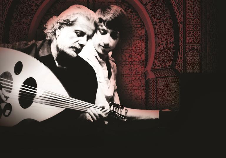 Marcel Khalifé playing his oud with Rami Khalifé behind him, looking over his shoulder as he plays piano