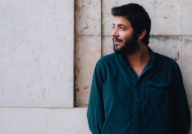 Salvador Sobral in front of a cream wall, looking to his right, wearing a dark blue shirt.