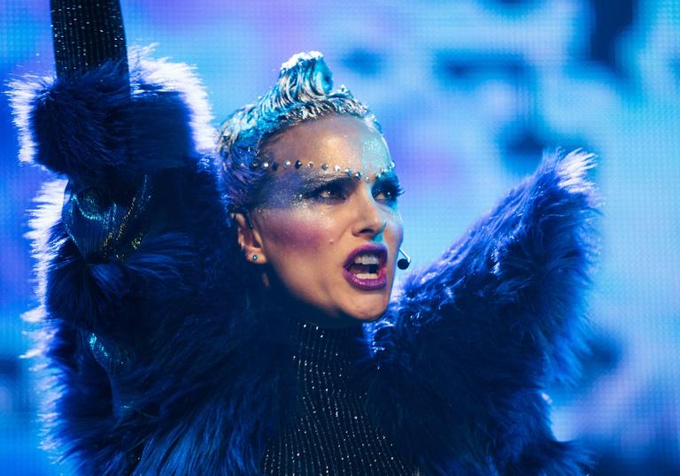 A bejewelled Natalie Portman in a fur jacket performing in a stadium