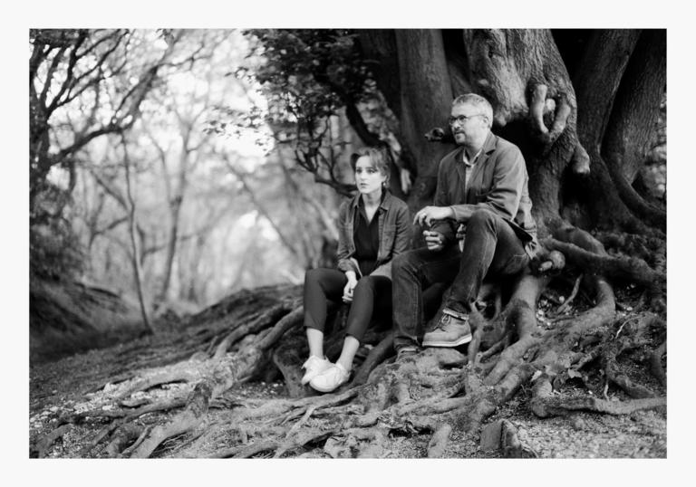 Hannah Peek and Will Burns sitting on the roots of a tree