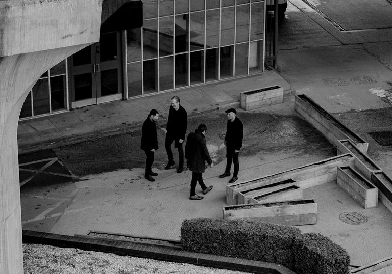 Ride standing in a group, in the surrounds of a brutalist building