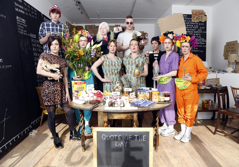 A group of people standing in a huddle around a circle table, wearing elaborate oufits.