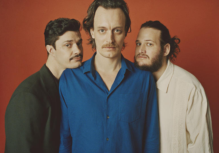 Efterklang standing together. Rasmus and Mads are resting their chins on Casper's shoulder