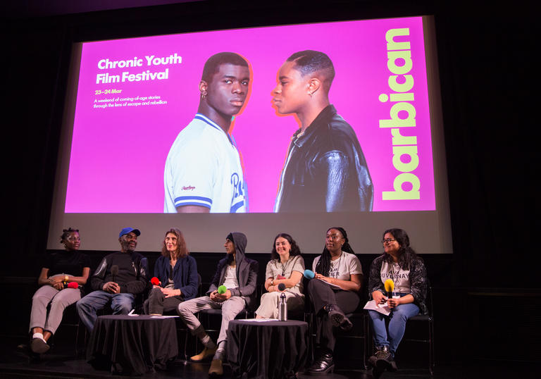 A panel of people sitting on stage with a large projection behind