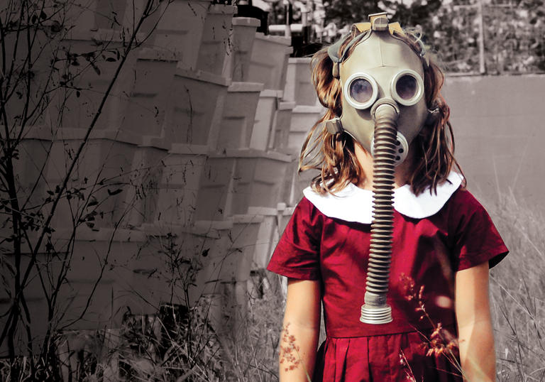 Young girl with gas mask standing in long grass