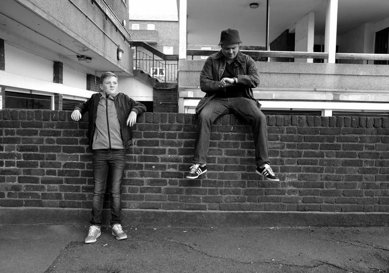 black and white image, two boys one sitting on a wall one standing next to the wall