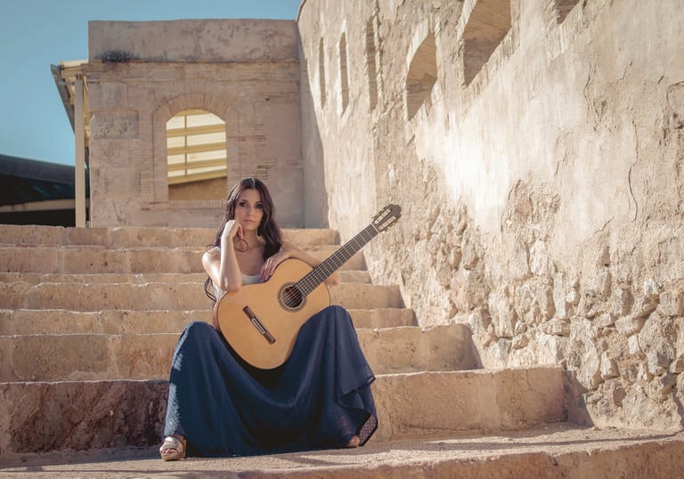 Guitarist Isabel Martínez sitting on stone steps in a sunny setting