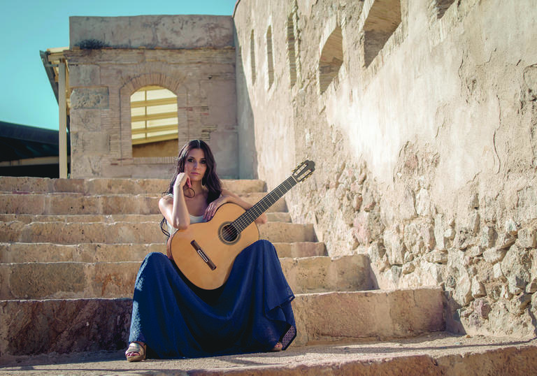 Guitarist Isabel Martínez sitting on stone steps in a sunny setting