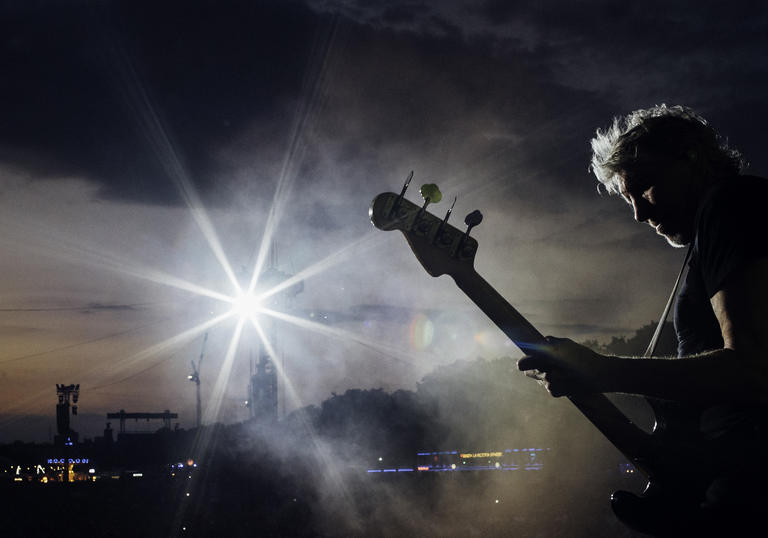 Roger Waters playing the guitar silhouetted against the sky