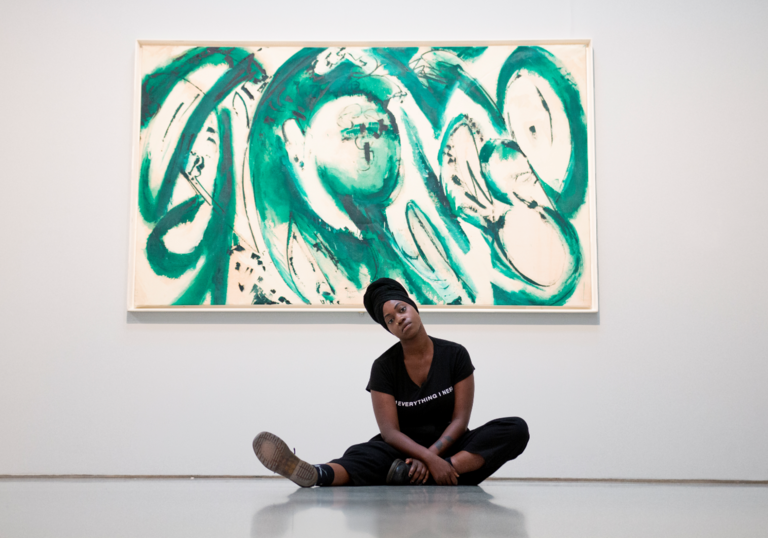image of young poet anita barton-williams sitting on the floor in front of a green painting by lee krasner