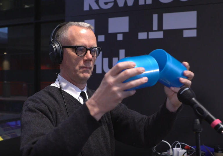 photo of a man with glasses holding a giant blue pill that is open in the middle