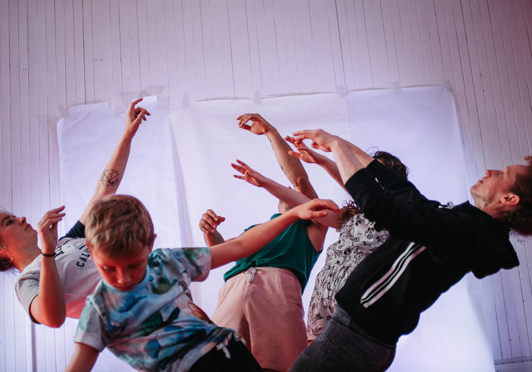 a group of adults and children are in motion as though they are falling backwards, arms in the air