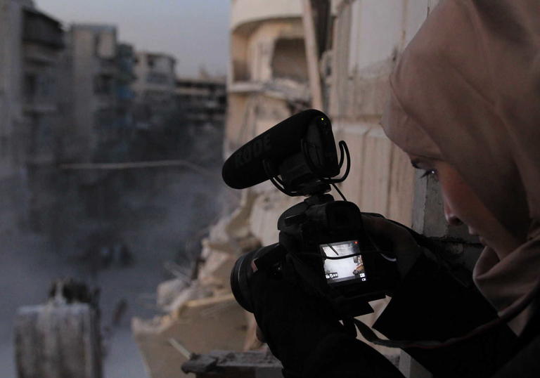 Waad with a camera pointing down to the street which is covered in dust and rubble