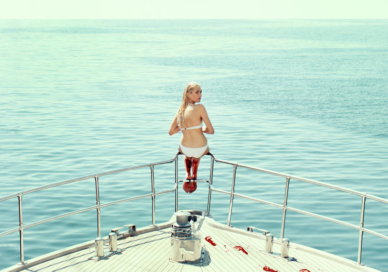 Victoria Carmen Sonne sitting at the front of a yacht looking towards the camera, blood dripping down her legs