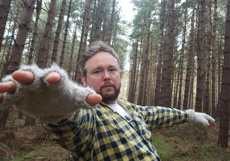 A man standing in the woods with an outstretched towards the camera