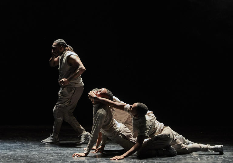 Four dancers on a stage. One is covering their own mouth while two others cover another's mouth