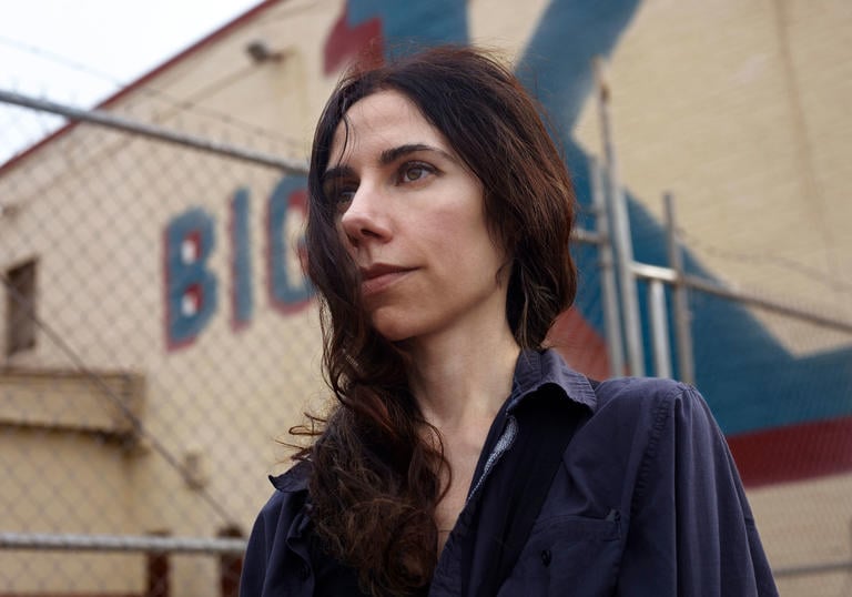 PJ Harvey in front of a cream building with a blue and red painted sign saying 'Big K'. 