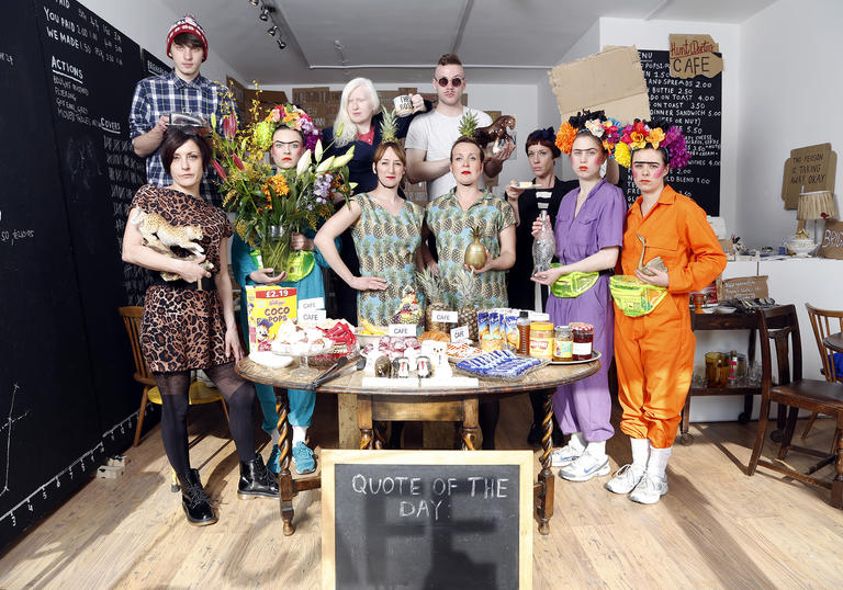 Group of people around a table full of food and objects.