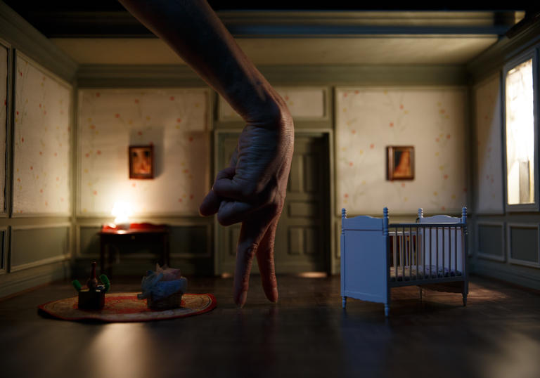 the set is a room with a crib in it, and a hand is posed as a person walking across the stage