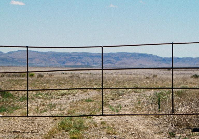 a fence set against a desert like backdrop with mountains and blue sky