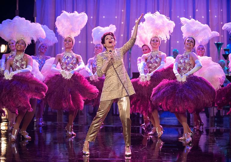 Renee Zellweger singing on stage as Judy Garland with dancers around her