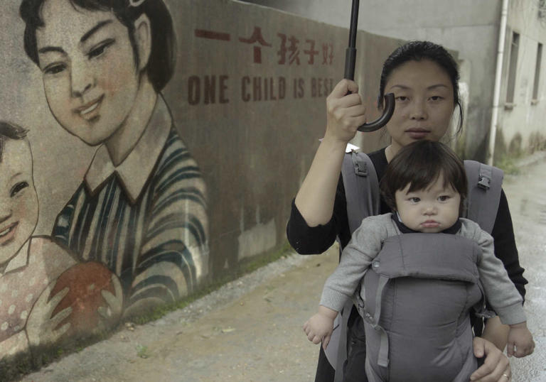 A woman holding her baby in front of a chinese mural