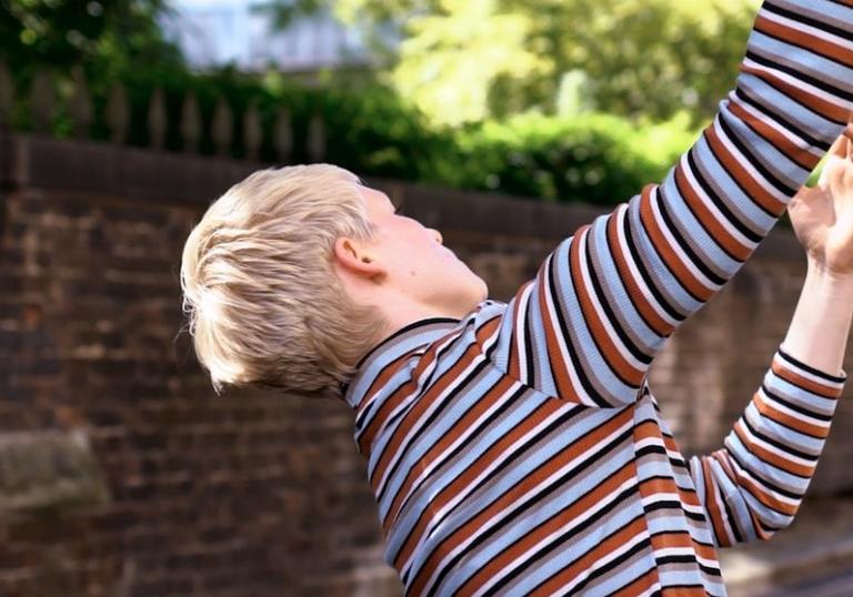 Blonde person in stripy polo neck dances down Leytonstone backstreet.