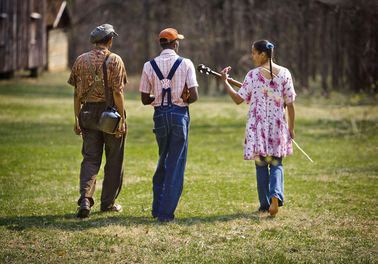 the Carolina Chocolate Drops trio from behind, as they walk with their instruments in a field