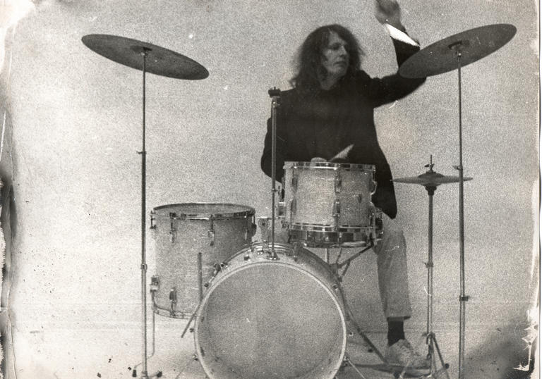 Klaus Dinger playing a classic drum kit against a bare wall