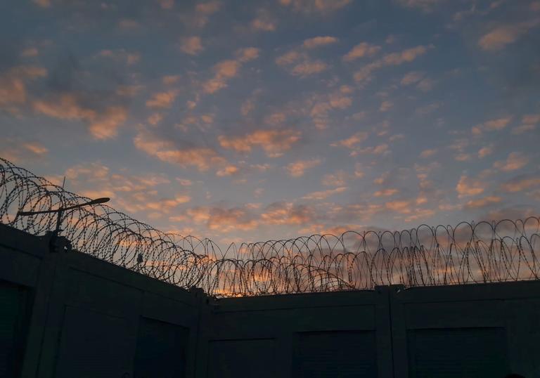 a wall with barbed wire on it against a sunset sky