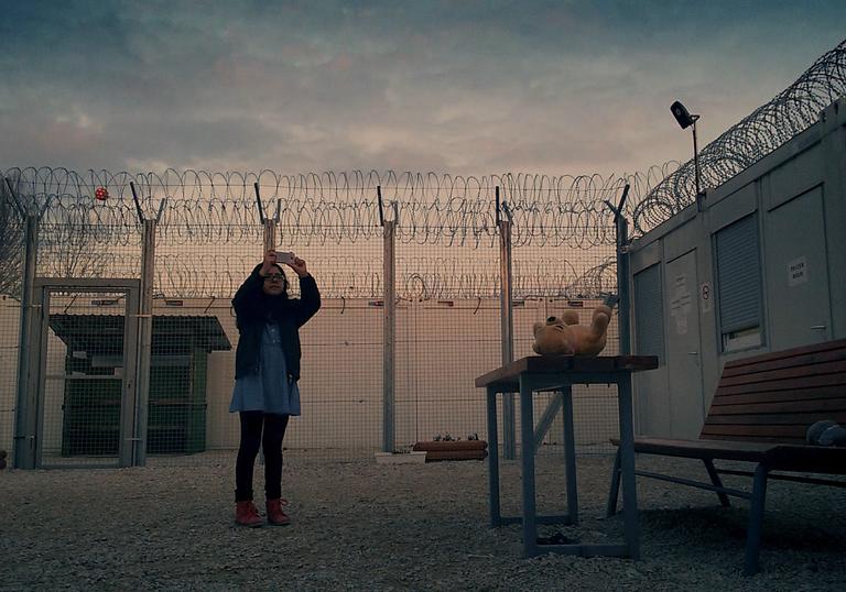 woman standing against the backdrop of a fence and sun setting sky