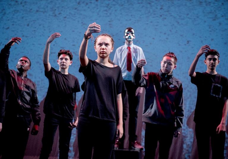 Six children all wearing black clothing, with their hands raised to the sky