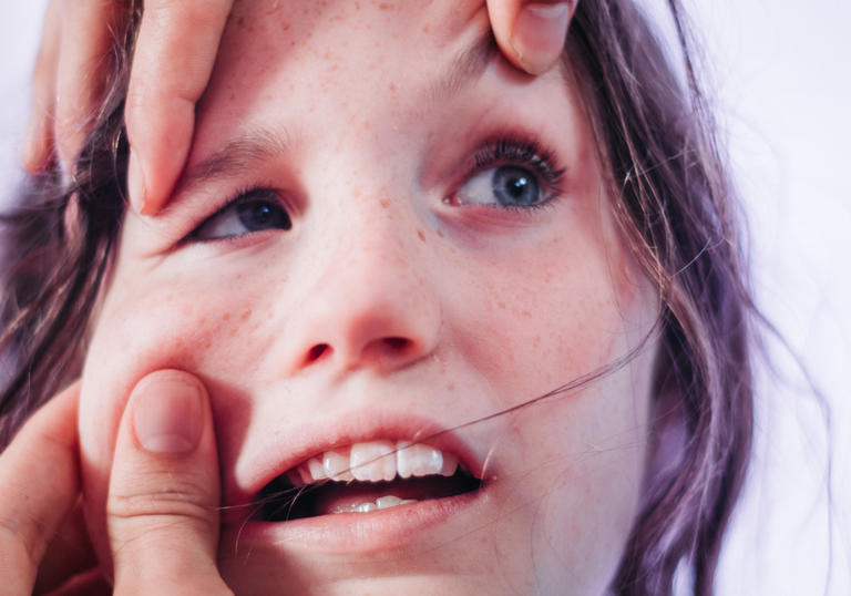 a photo of a child with someone's hands on her face, pulling at their skin