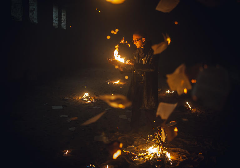 paper falls from ceiling , man burns paper, fire pit on the ground