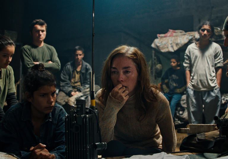 A young woman and some children wait attentively at a radio in the film Monos