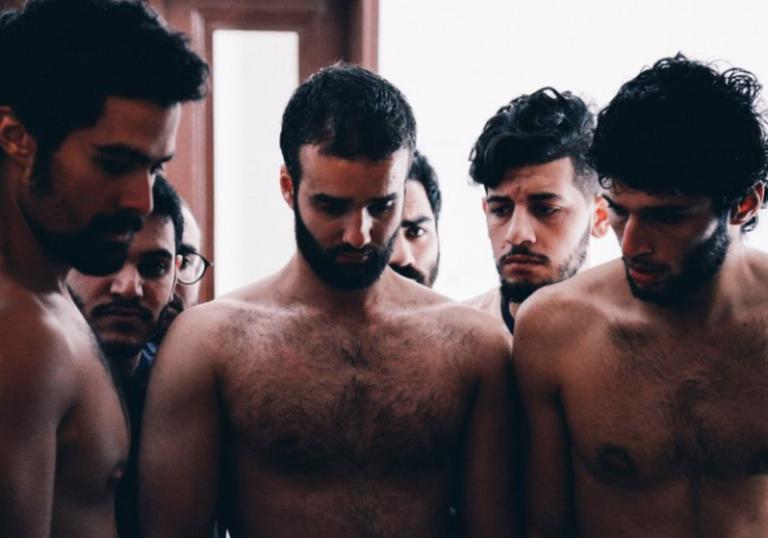 a group of topless men stand looking at the floor