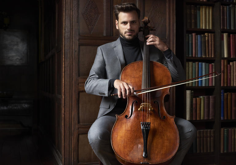 Stjepan Hauser playing cello in front of bookcase