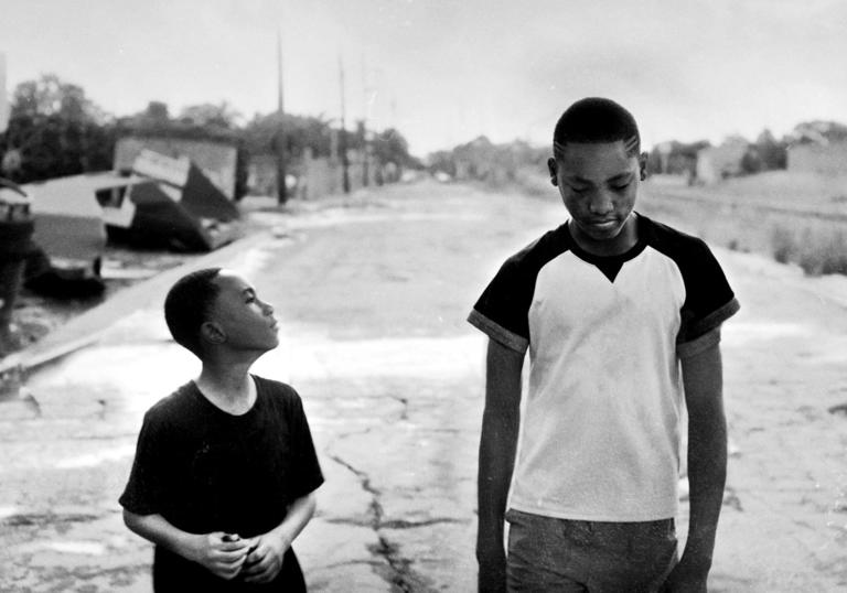 two boys walking down the street in black and white