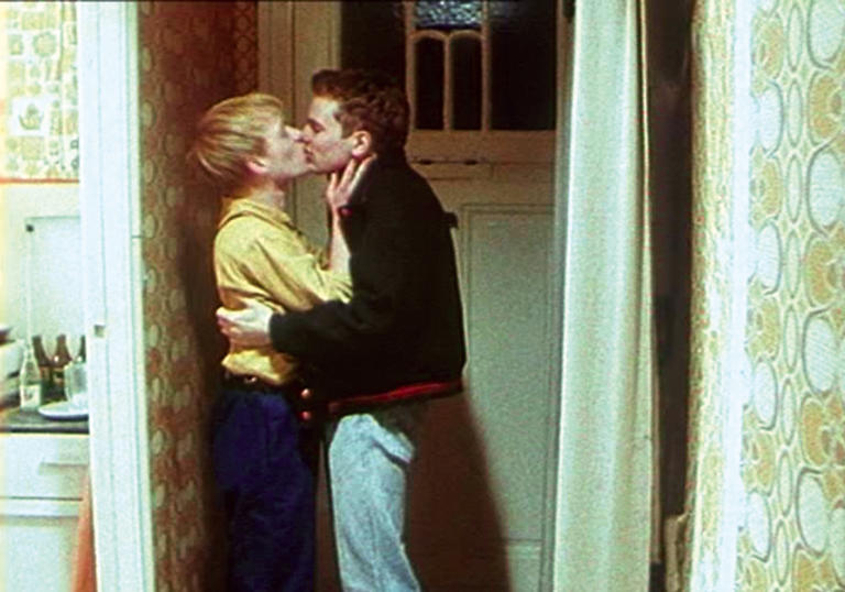 Two men kiss in a 1980s hallway in East Germany, in Wieland Speck's Westler