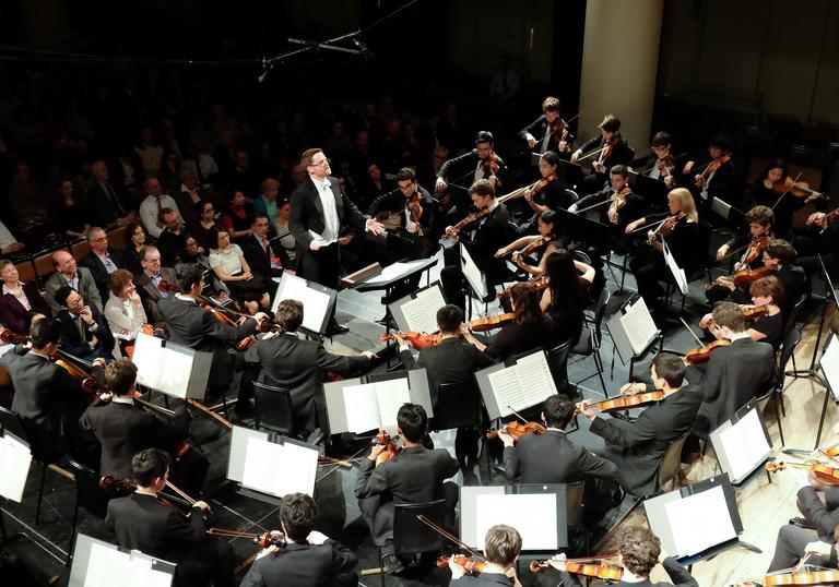 Orchestral string section playing music with a conductor