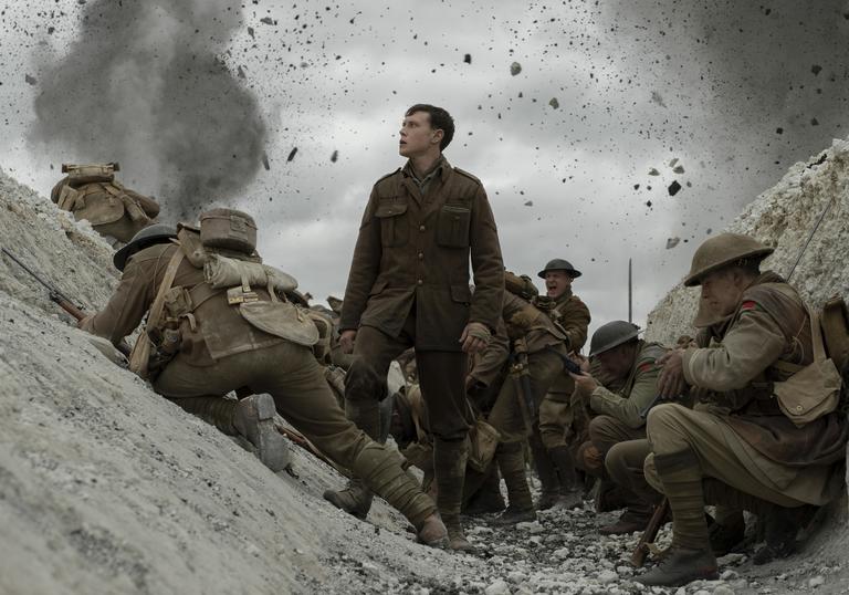 George MacKay stands in the trench surrounded by explosions and other men