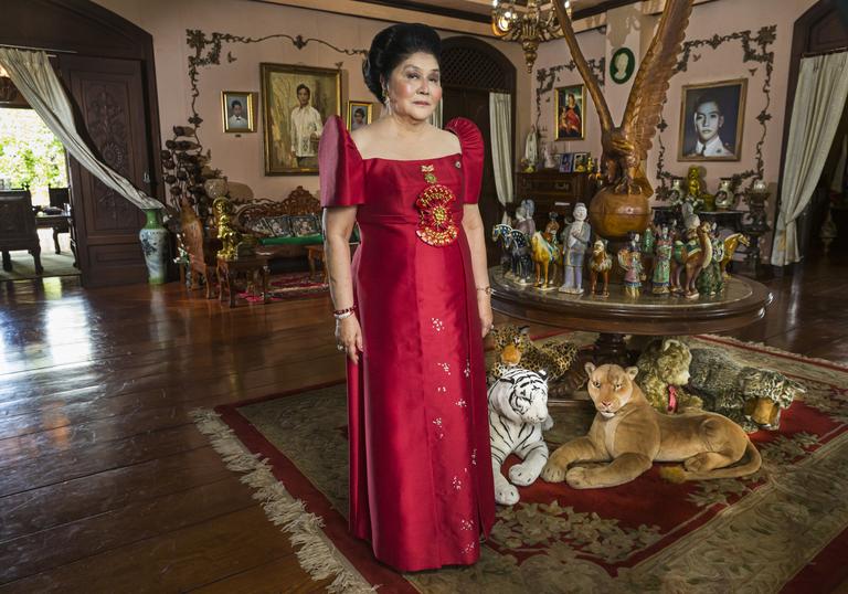 Imelda Marcos standing in an opulent room wearing a red dress