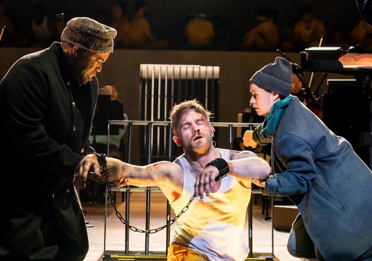 A jailer and his assistant helping a prisoner in chains out of cell