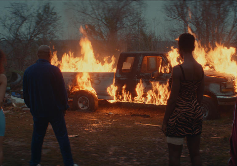 people standing in front of a burning car