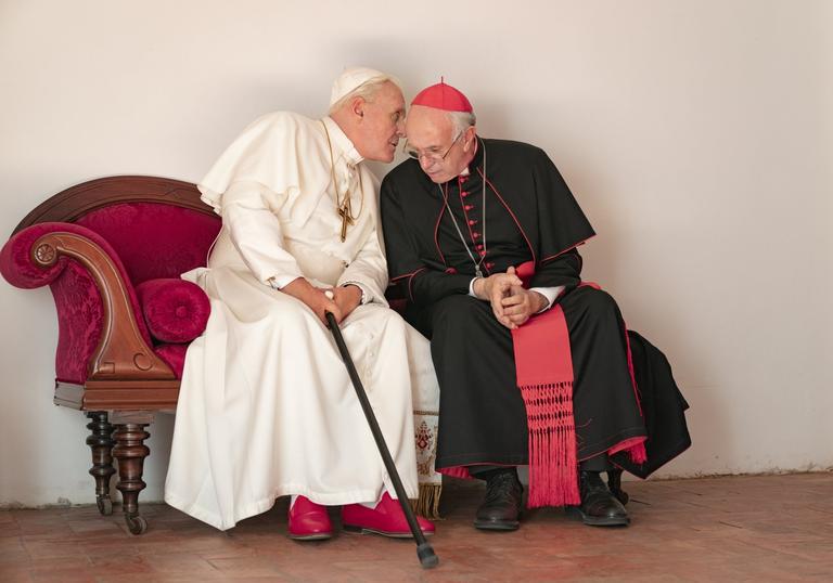 the two popes, Francis and Benedict sit next to each other with one whispering in the other's ear