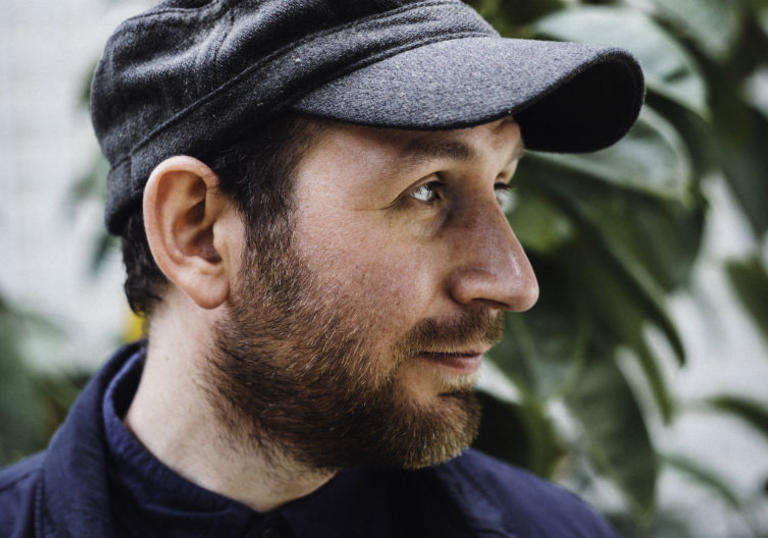 photo of Matthew Halsall's face. He has a beard and is wearing a cloth hat. In the background is an out of focus green plant