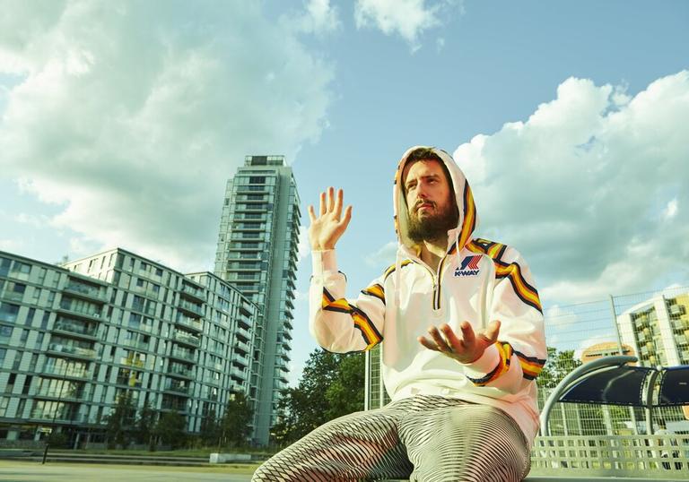 Danalogue sitting amongst glass buildings, gesturing with his hands