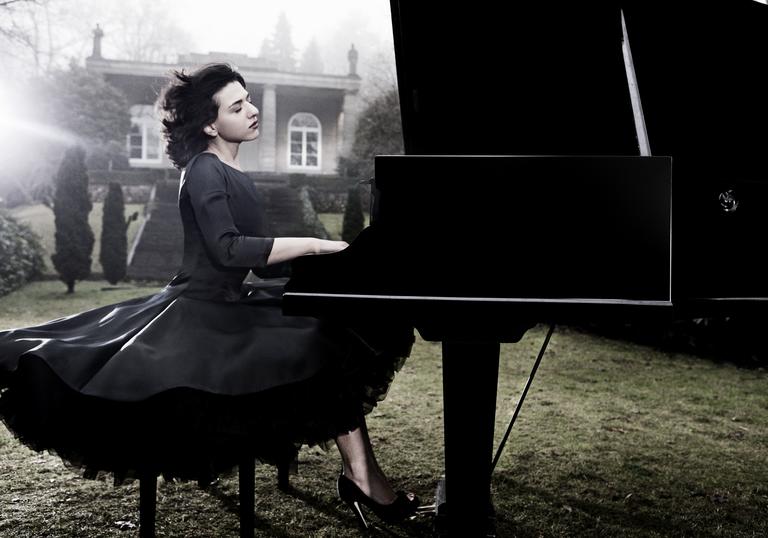 An ethereal image of Khatia in a stately garden with wind in her hair, expertly playing the piano with great emotion