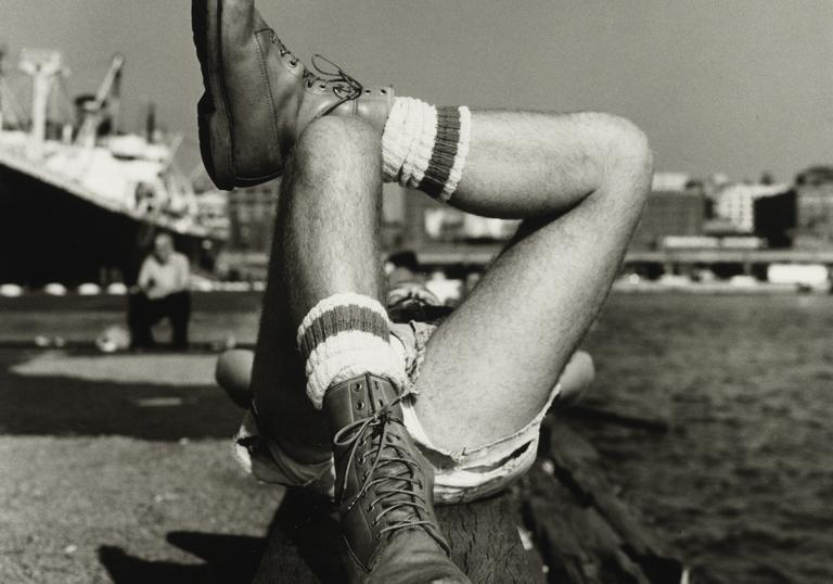 An black and white image of a man's crossed legs, lying in a harbour