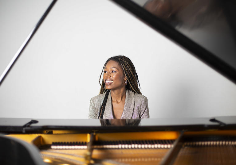 Am image of Isata sitting by the piano and smiling 